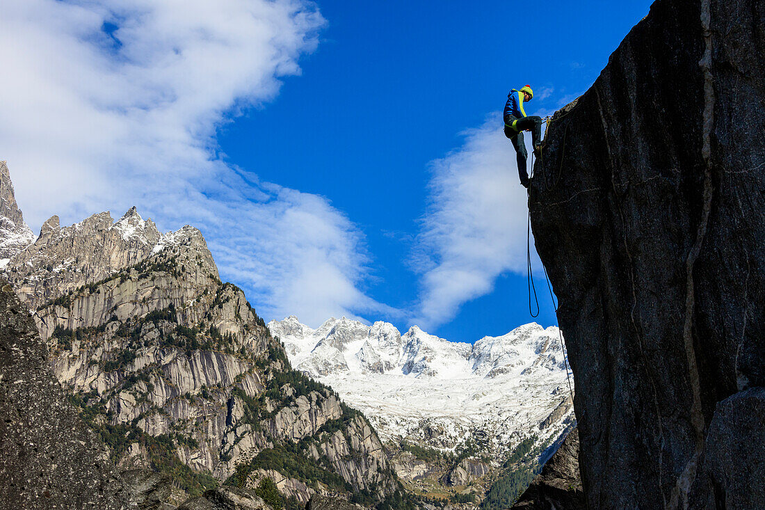 Climber on steep rock face in the background blue sky and snowy peaks of the Alps, Masino Valley, Valtellina, Lombardy, Italy, Europe