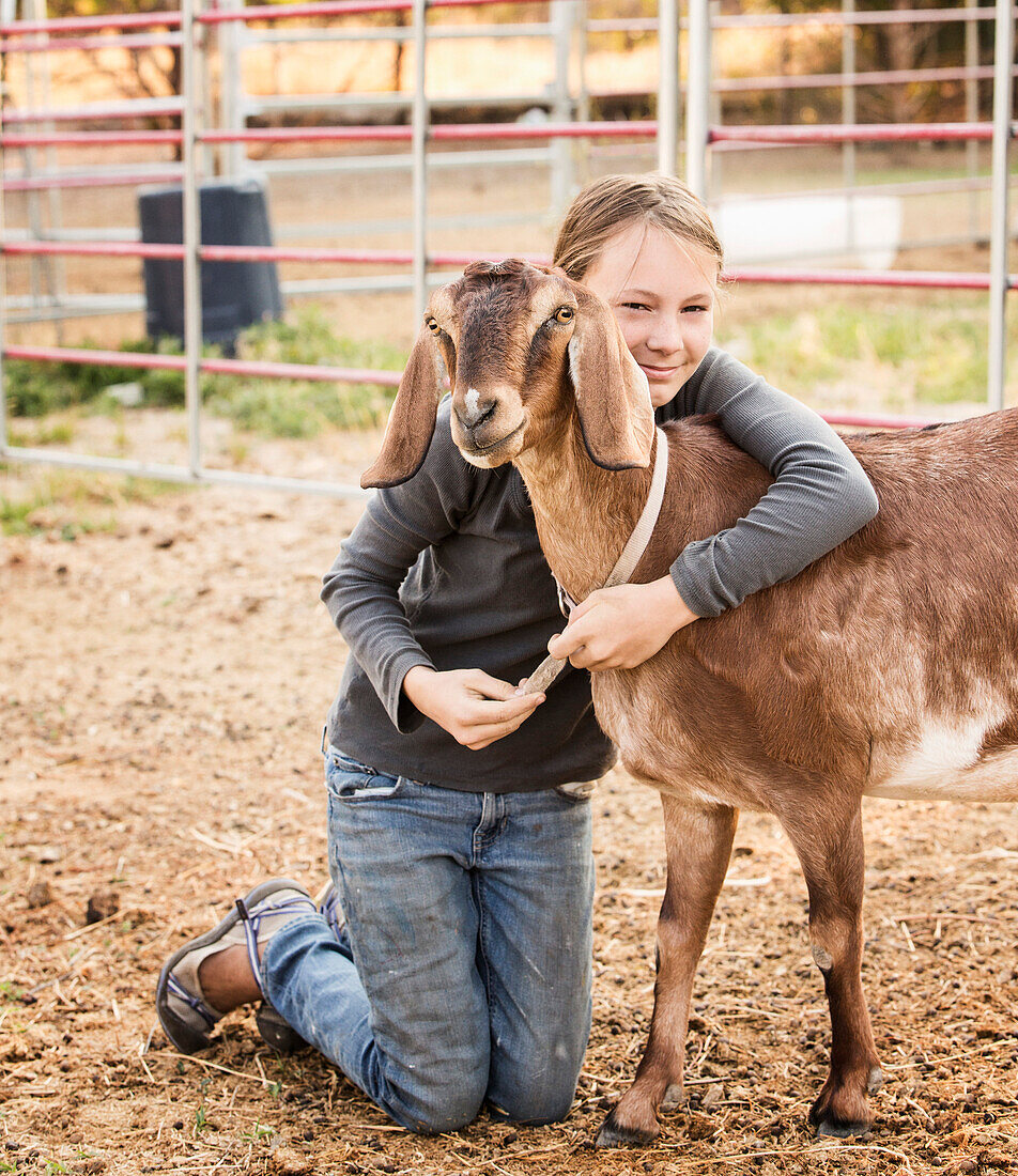 Smiling girl hugging goat on farm