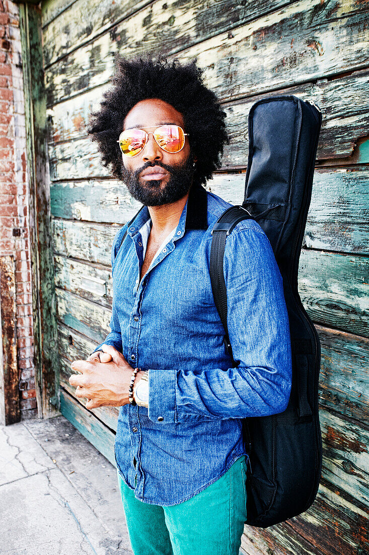 Mixed race musician carrying guitar outdoors