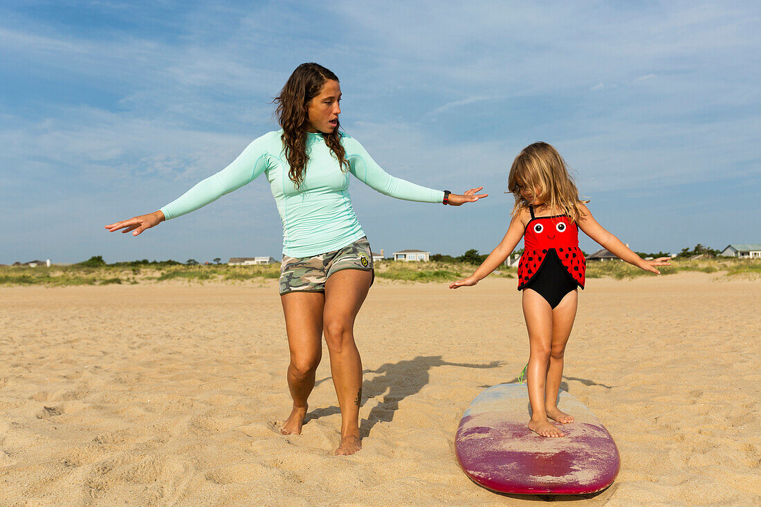 Mother teaching daughter to surf at beach