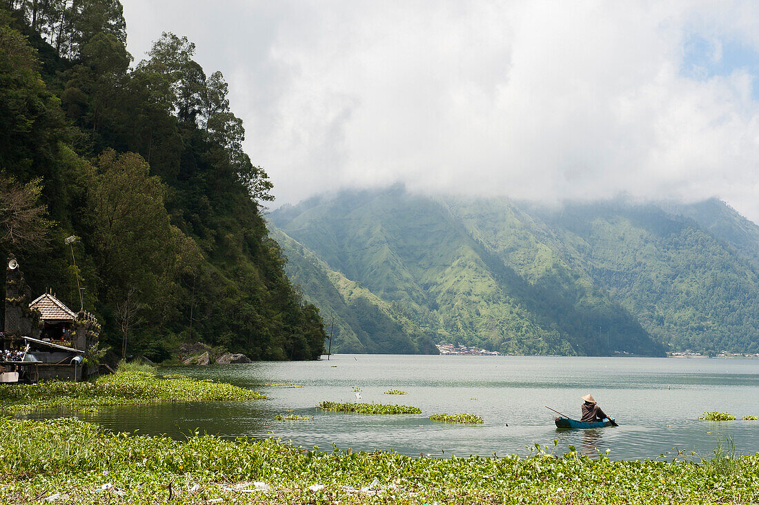 Fisherman rowing canoe on still rural lake