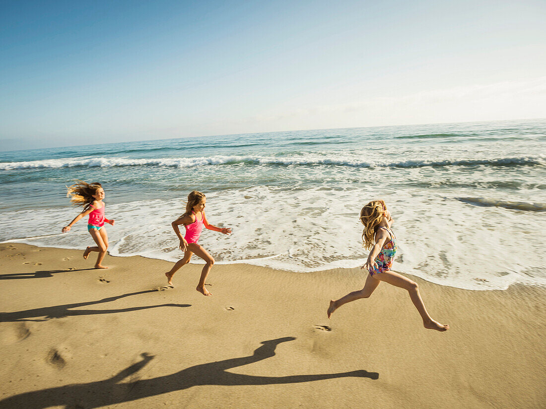 Caucasian sisters running on beach
