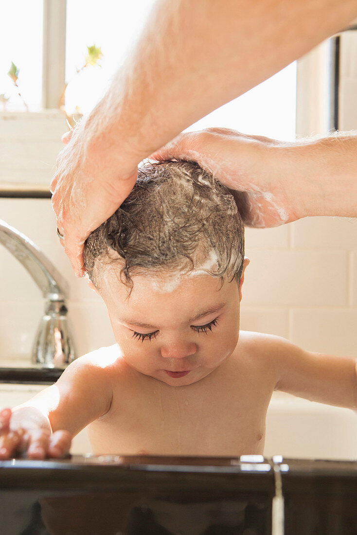 Father washing baby son in kitchen sink