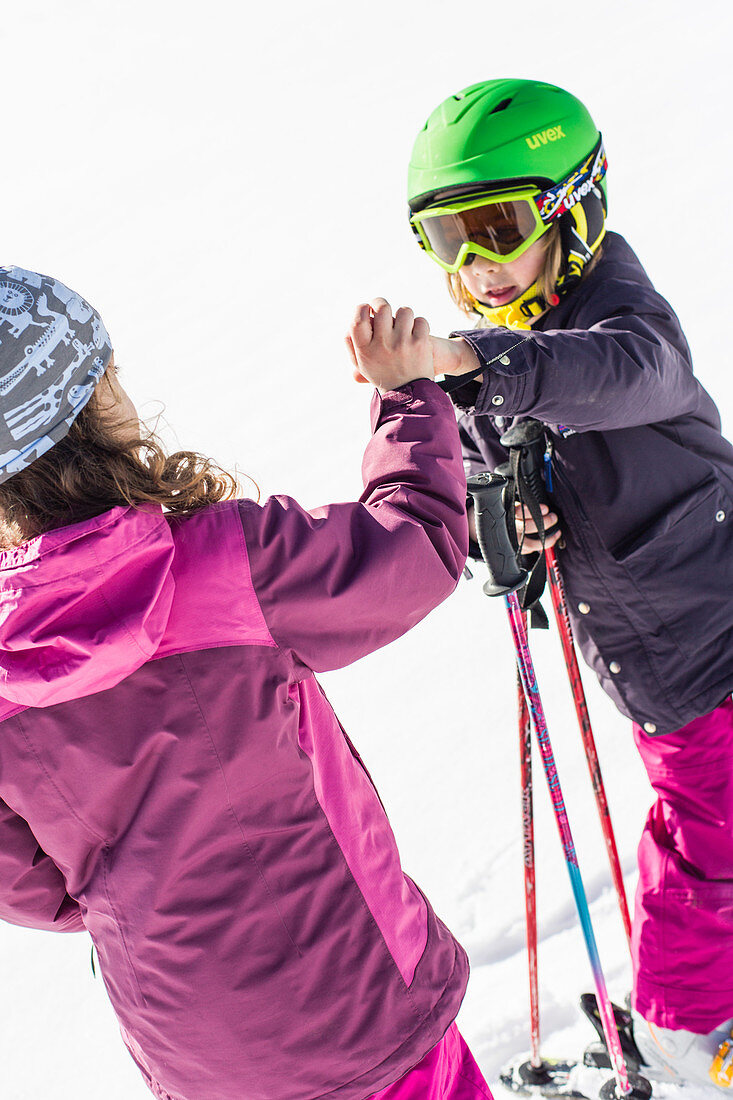 girl and boy giving a high five whilst skiing, Pfronten, Allgaeu, Bavaria, Germany