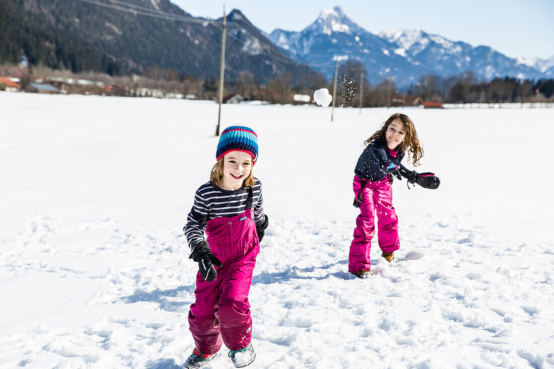 Mädchen schmeißt Schneeball auf Jungen bei einer Schneeballschlacht im Winter, Pfronten, Allgäu, Bayern, Deutschland