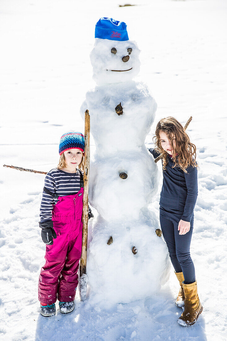 Mädchen und Junge bauen einen Schneemann im Winter, Pfronten, Allgäu, Bayern, Deutschland