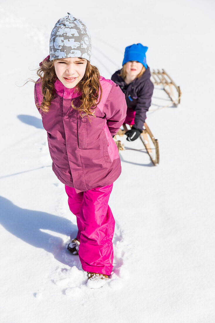 Girl pulling boy on their sleds, Pfronten, Allgaeu, Bavaria, Germany