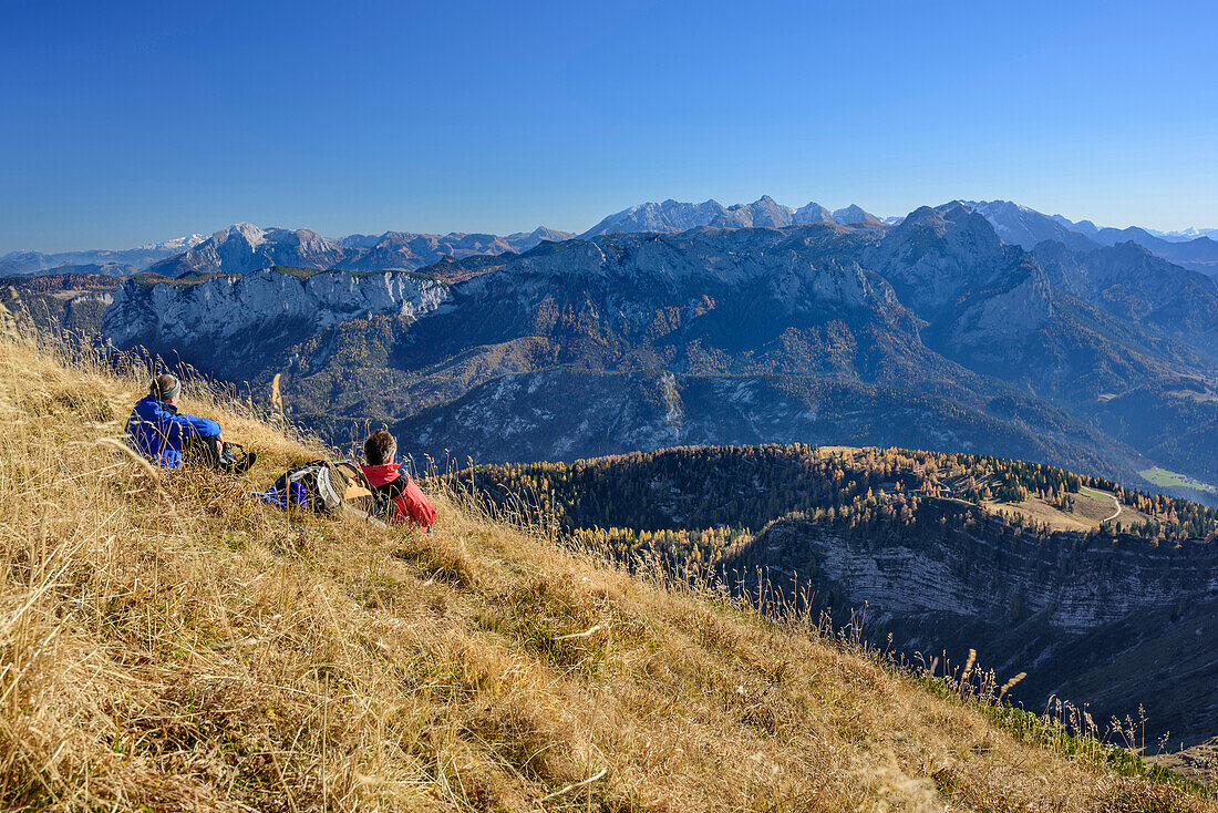 Two persons sitting at Sonntagshorn and looking towards Berchtesgaden Alps, Sonntagshorn, Chiemgau Alps, Salzburg, Austria