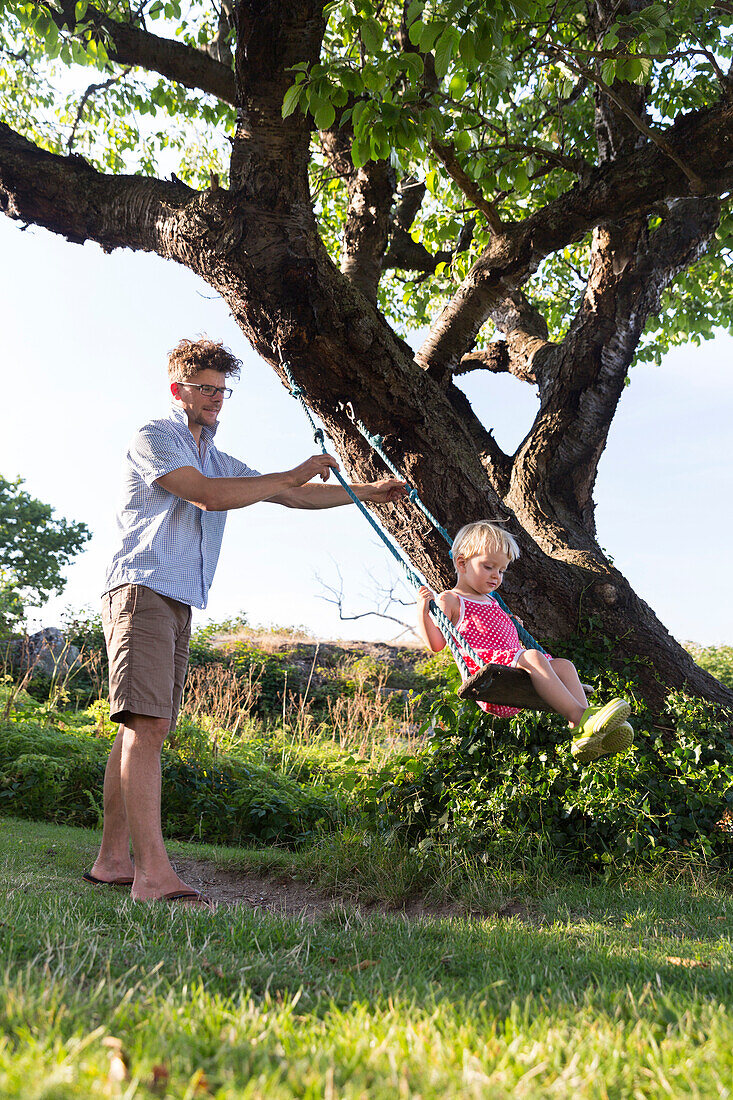 Father pushing young daughter on the swing, Summer, Baltic sea, MR, Bornholm, Svaneke, Denmark, Europe