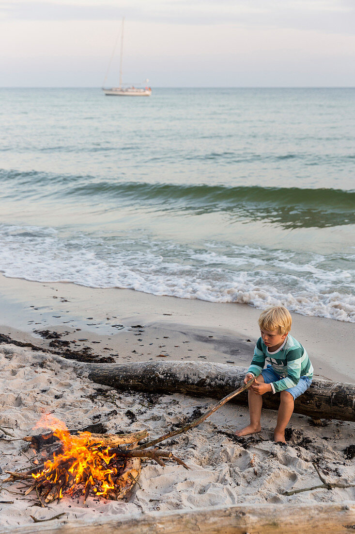 Five year old boy sitting around the campfire, adventure, sailing boat, dream beach between Strandmarken und Dueodde, sandy beach, summer, Baltic sea, Bornholm, Strandmarken, Denmark, Europe, MR