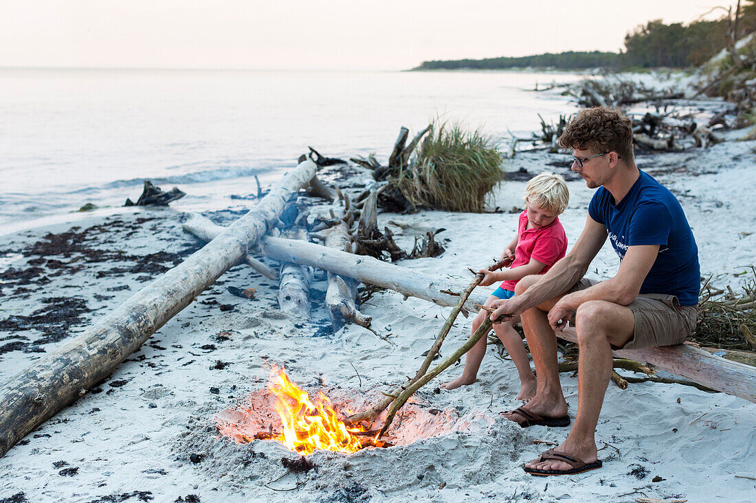 Five year old boy sitting with his father around a campfire, adventure, dream beach between Strandmarken und Dueodde, sandy beach, summer, Baltic sea, Bornholm, Strandmarken, Denmark, Europe, MR