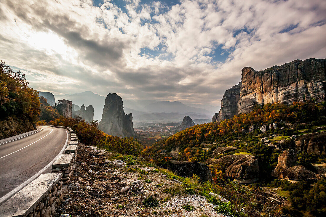 Landscape of rugged cliffs, road, autumn foliage and Monastery Rousanou in the distance, Meteora, Greece
