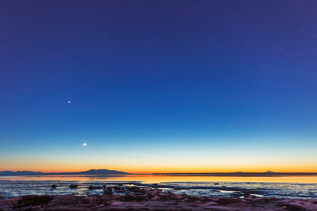 The moon rises above Mount Susitna on a clear winter night, sea ice visible in the foreground, Anchorage, Alaska, United States of America