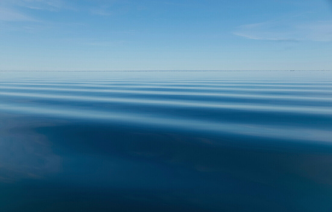 Surface of blue water with slight ripples and blue sky with horizon in the distance