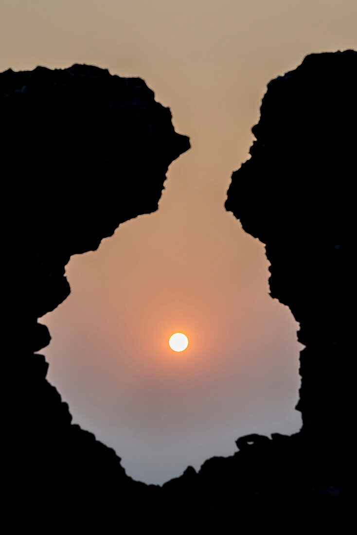 Sunrise seen through a hole in an old stone wall without a cloud in the sky, Rampura Bas Ganwar, Rajasthan, India