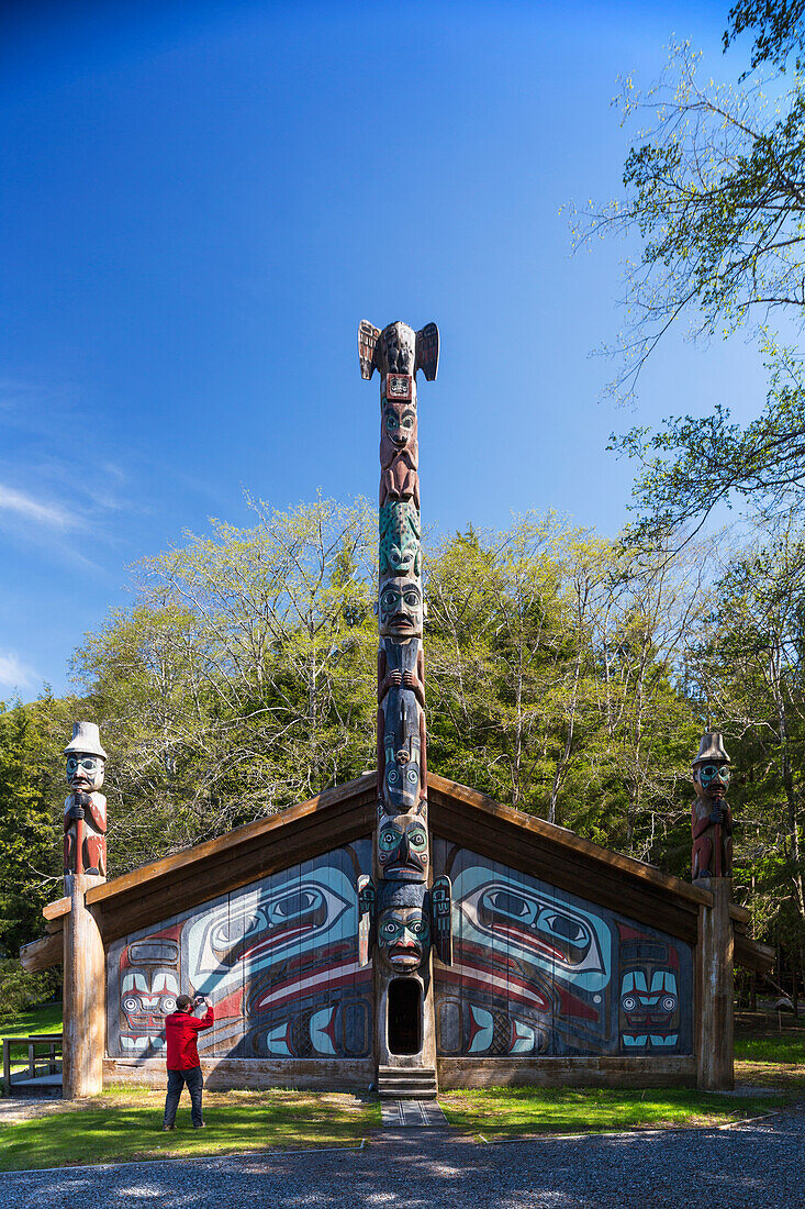 Tourist photographs a totem pole and a clan house, Totem Bight Historic State Park, Ketchikan, Southeast Alaska, USA, Spring