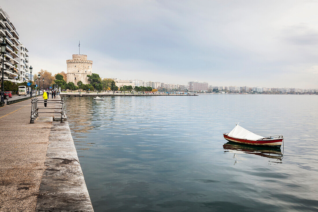 A lone boat moored in the water along the waterfront with White Tower in the distance, Thessaloniki, Greece