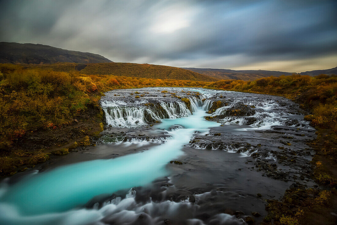 Long exposure of water flowing over rock in a stream and dark clouds in the sky, Bruarfoss, Iceland
