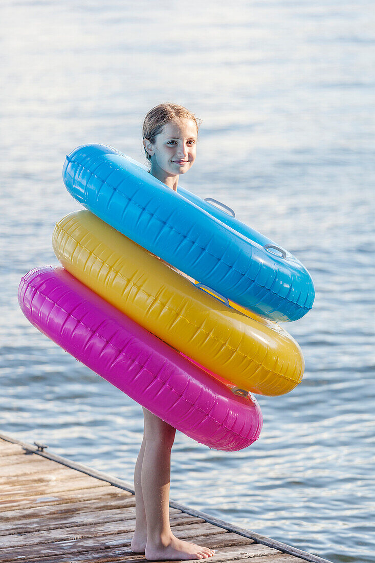 Girl standing on edge of dock by Balsam Lake wearing colorful inflatable rings, Ontario, Canada