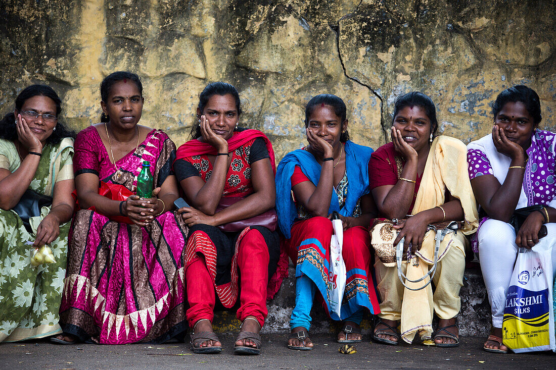Sechs Inderinnen sitzen an einer Mauer, Thiruvananthapuram, Kerala, Indien