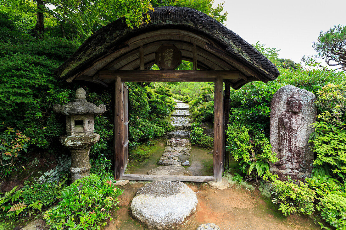 Okochi Sanso Villa, cobbled path through a wooden gateway in the verdant stroll garden in summer, Arashiyama, Kyoto, Japan, Asia