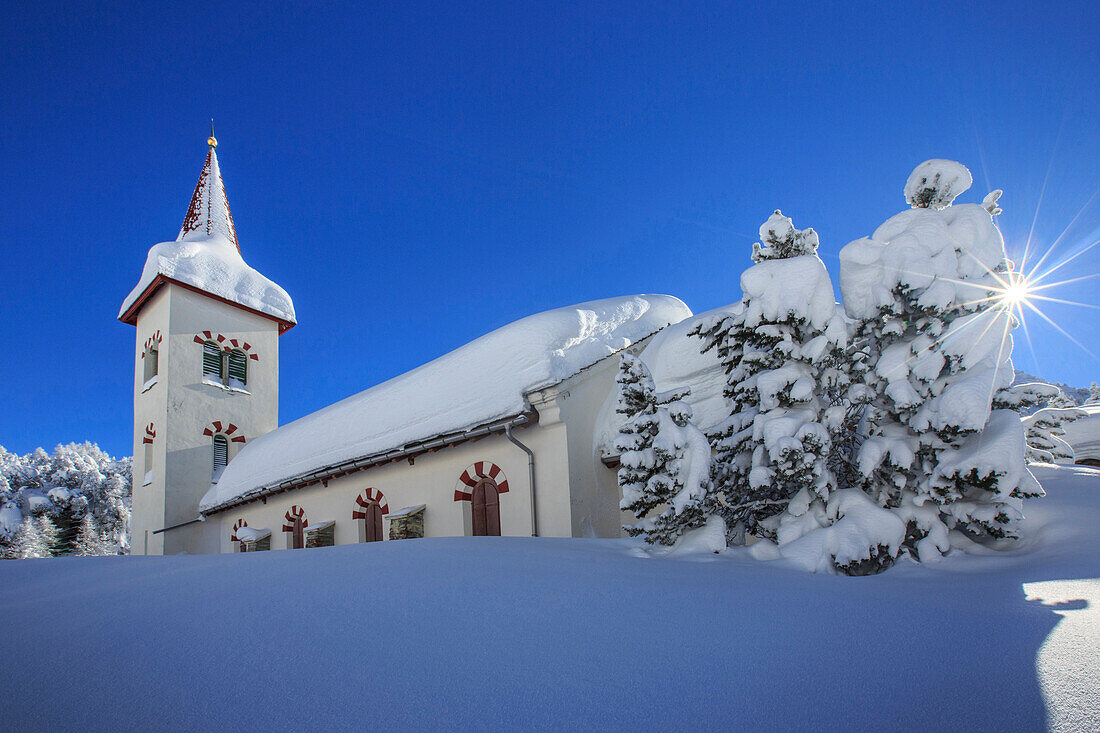 Rays of winter sun illuminate the snowy landscape and the typical church, Maloja, Engadine, Graubunden Grisons Canton, Switzerland, Europe
