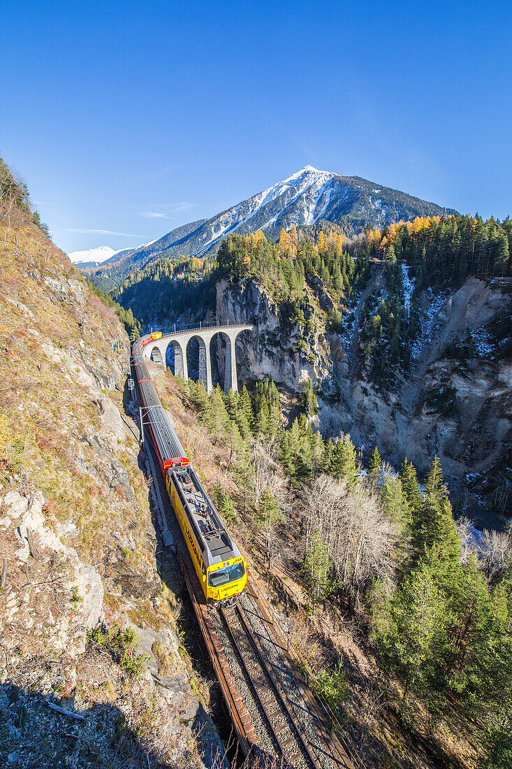 Bernina Express passes over the Landwasser Viadukt surrounded by colorful woods, Canton of Graubunden, Switzerland, Europe