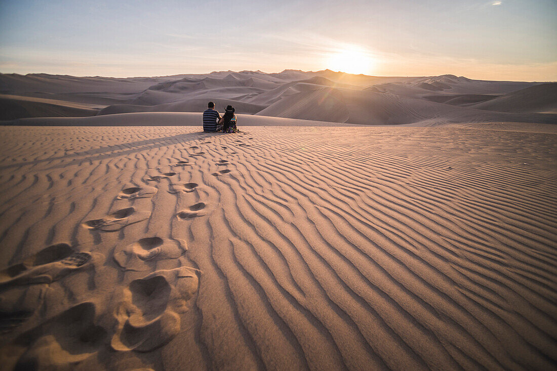 Couple watching the sunset over sand dunes in the desert at Huacachina, Ica Region, Peru, South America