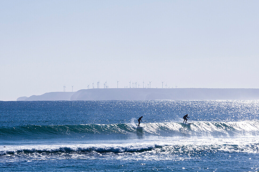Two stand up paddle boarders brave the cold Marrawah waters on the West Coast of Tasmania durng winter. The Woolnorth windfarm can be seem out in the distance.