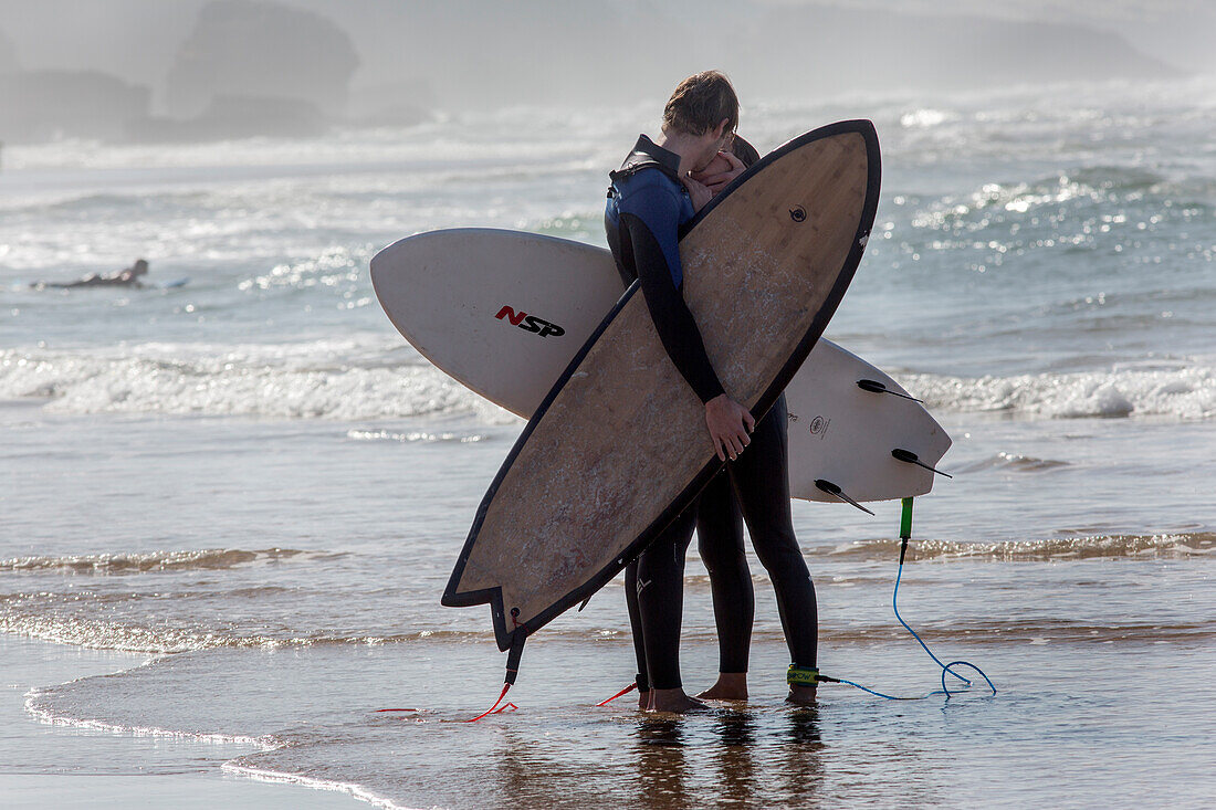 A young couple kisses on the beach with surfboards in Morocco.