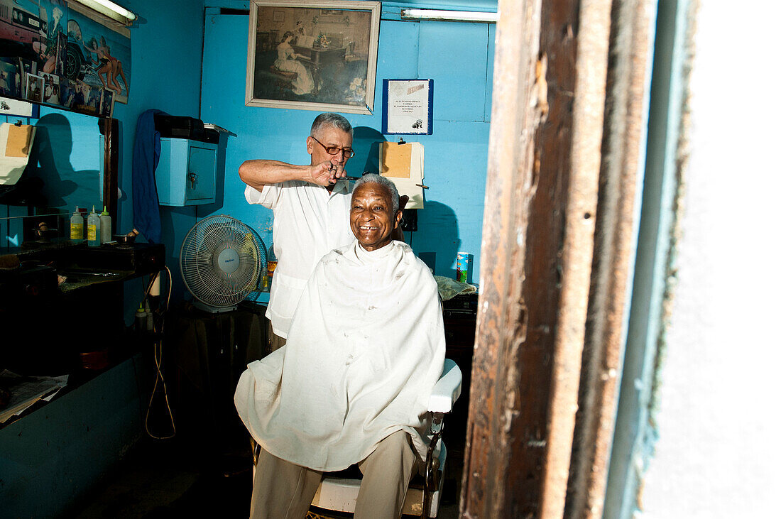 An elderly man smiles while getting his hair cut in a barber shop in Havana, Cuba.