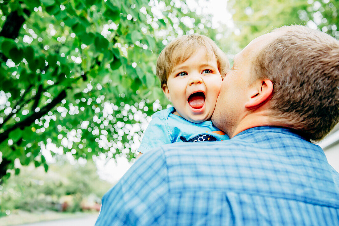 Father kissing cheek of baby son outdoors
