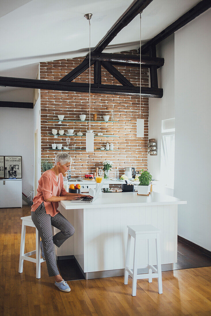 Older Caucasian woman using laptop in kitchen