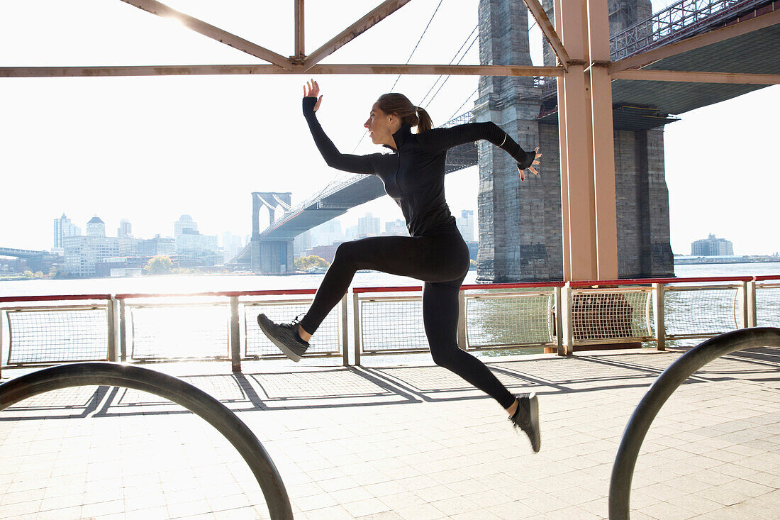 Caucasian runner jumping on waterfront, New York, New York, United States