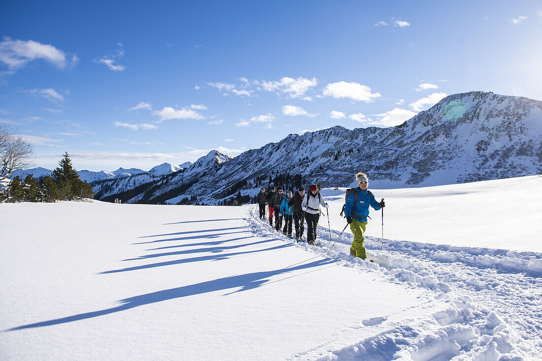 Ankommende Gruppe Schneeschuhwanderer mit Schatten im Schwarzwassertal bei Sonnenschein und Schnee, Vorarlberg, Österreich