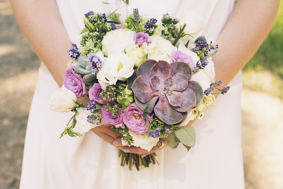 Bride holding bouquet of flowers and succulent plants, cropped