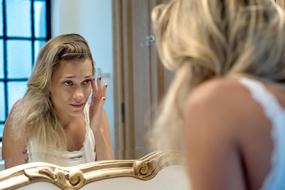 Woman looking bleary-eyed at self in bathroom mirror