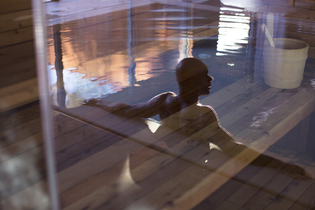 Man relaxing in swimming pool, reflected on glass door