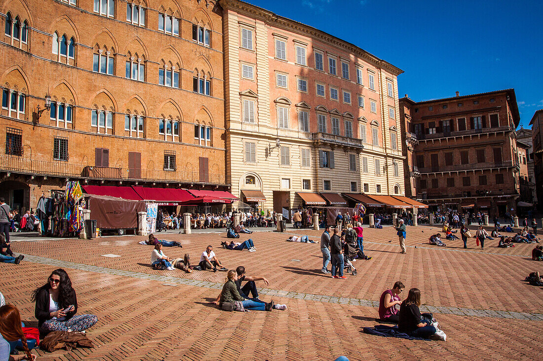 touristes et passants prenant le soleil sur la piazza del campo de sienne, sienne, italie, union europeenne