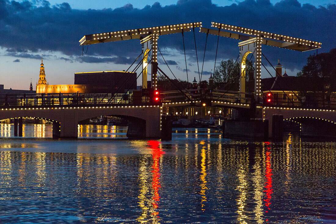 magere brug bridge and canals lit up at night in front of the national opera and ballet, amstel, amsterdam, holland