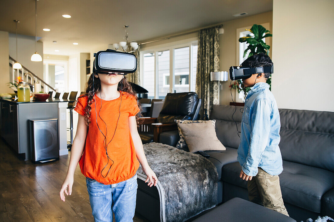 Mixed race children using virtual reality goggles in living room