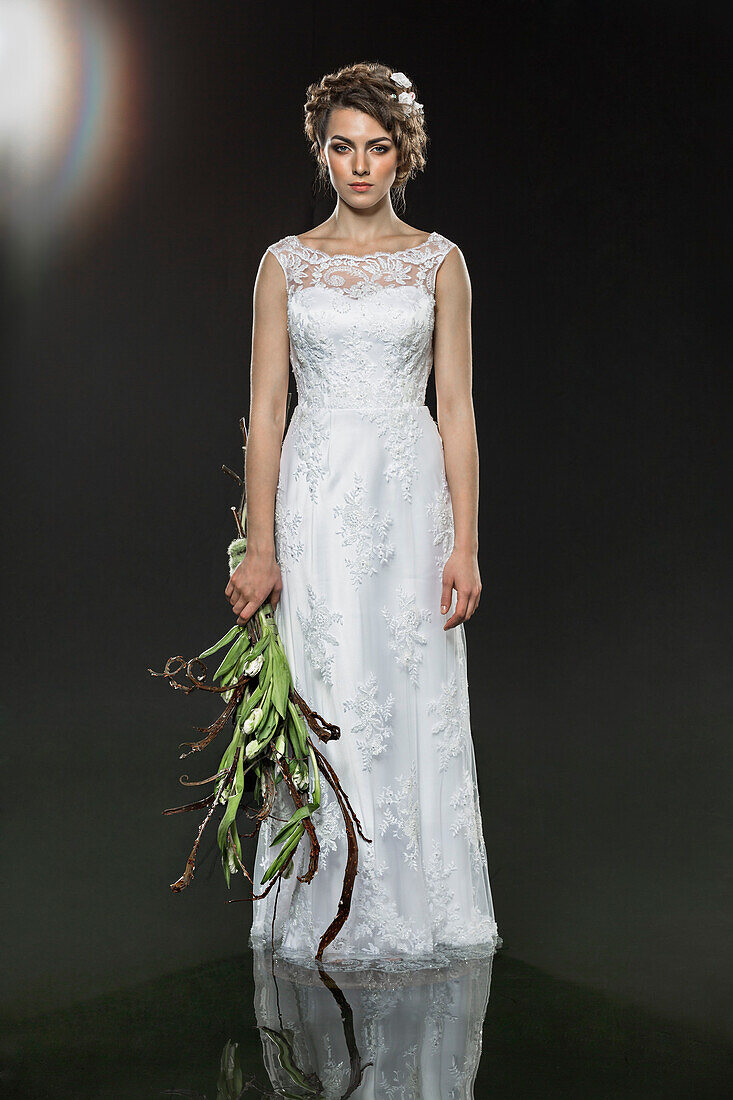 Portrait of sad young bride holding wilted bouquet while standing in water against gray background