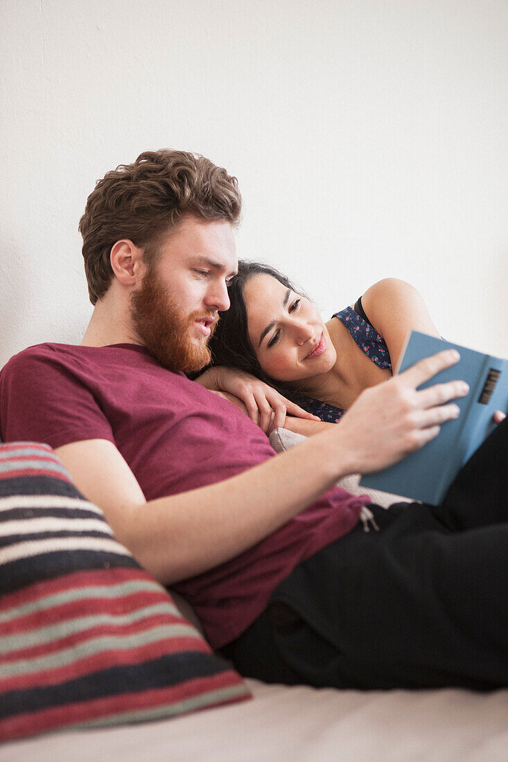 Young man reading book for woman in bed