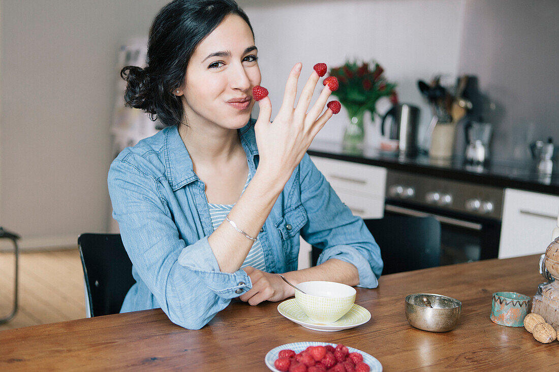 Portrait of happy young woman holding raspberries on fingers at home