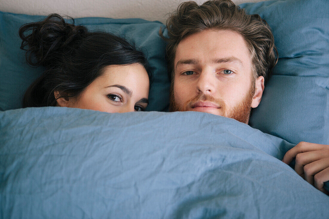 Portrait of loving young couple under duvet in bed