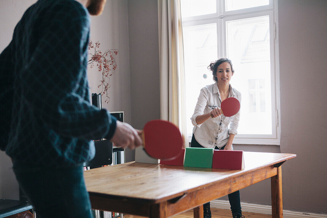 Young woman playing table tennis with man at home