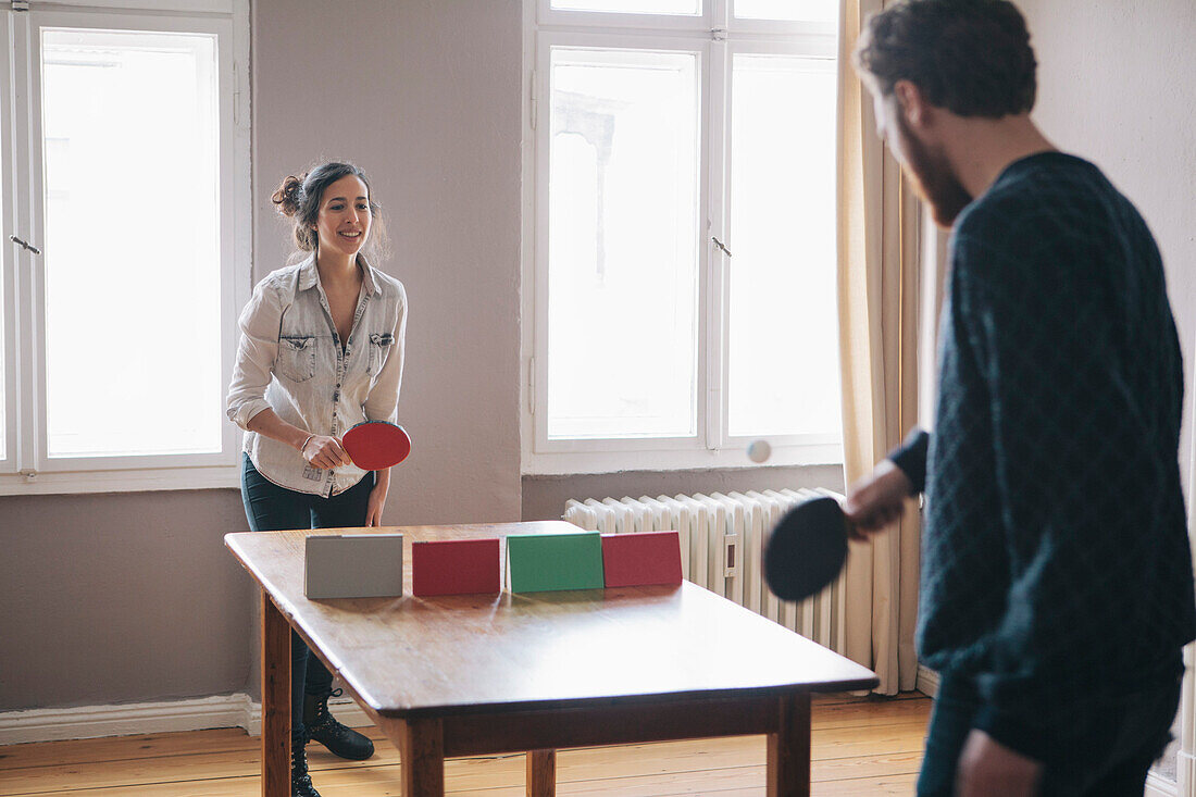 Young woman playing table tennis with man at home