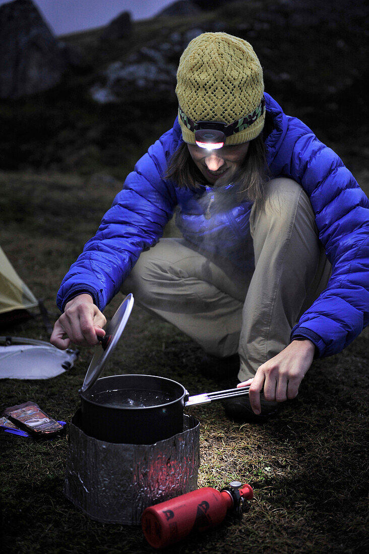 Woman hiker prepares a meal at camp during a backpacking trip to Reed Lakes in the Talkeetna Mountains near Palmer, Alaska August 2011.