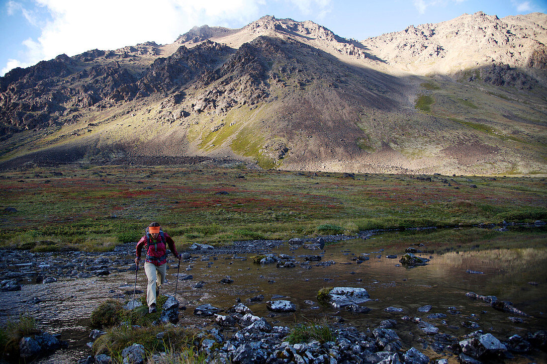 Female hiker crosses the North Fork Campbell Creek below Long Lake in the Chugach Mountains north of Anchorage, Alaska August 2011.