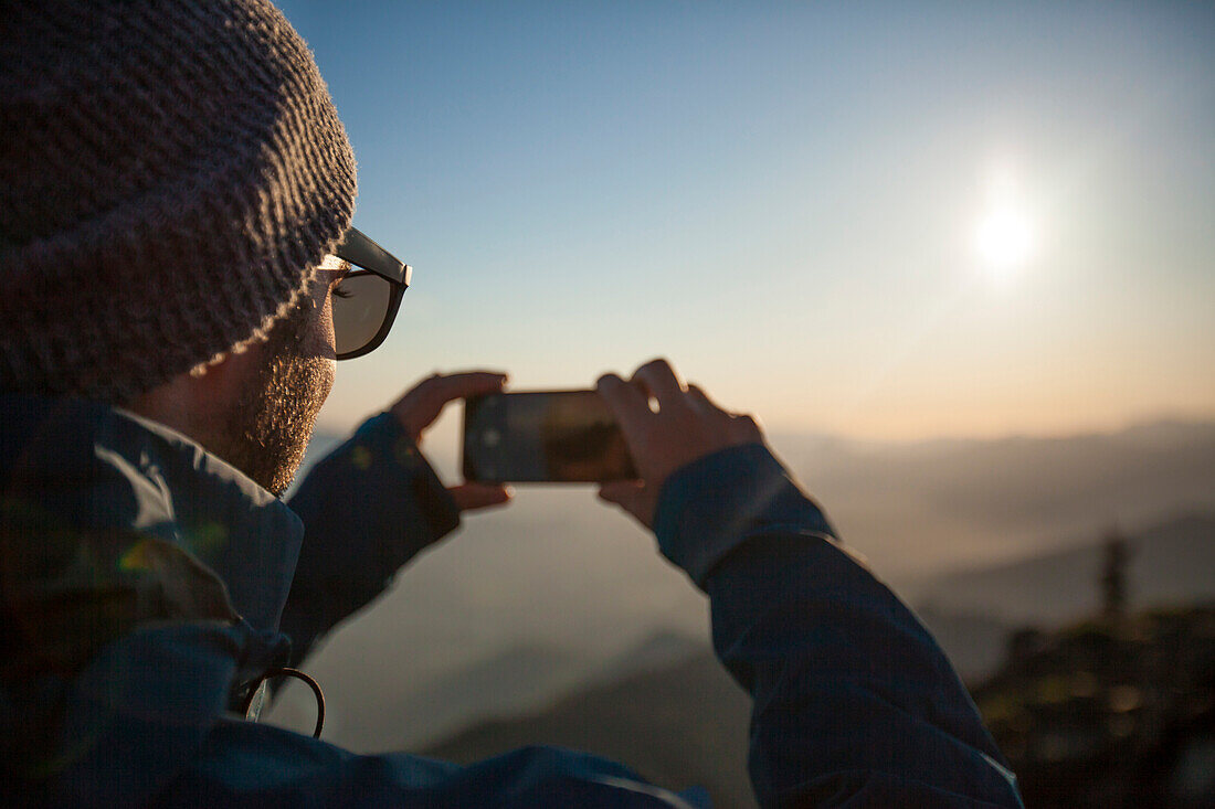 A man uses his phone to snap a photo of the view from the summit of Sauk Mountain in the North Cascades, Washington.